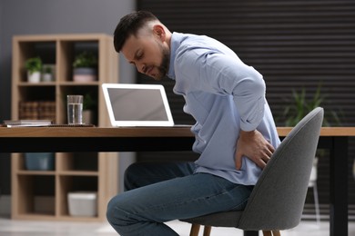 Man suffering from back pain while working with laptop in office. Symptom of poor posture