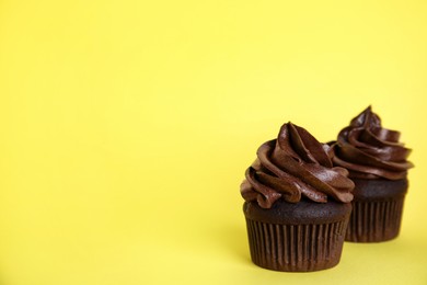 Delicious chocolate cupcakes with cream on yellow background. Space for text