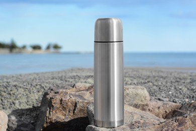 Photo of Metallic thermos with hot drink on stone near sea