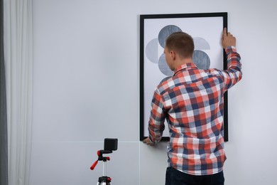 Man using cross line laser level for hanging painting on light wall, back view