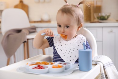 Cute little baby eating food in high chair at kitchen