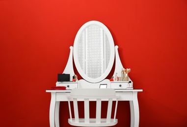 Elegant dressing table with makeup products and chair on red background