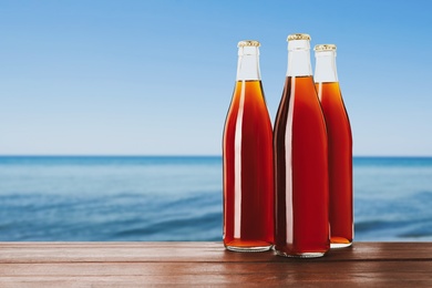 Bottles of delicious kvass on wooden table near sea. Space for text