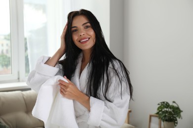 Beautiful young woman in bathrobe drying hair with towel indoors