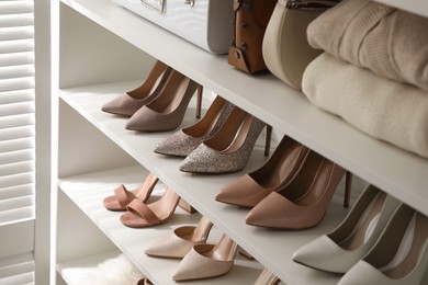 Stylish women's shoes, clothes and bags on shelving unit in dressing room