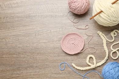Flat lay composition with knitting threads and crochet hook on wooden table, space for text
