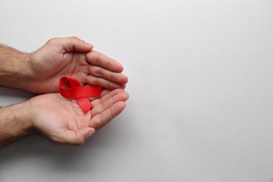 Man holding red awareness ribbon on white background, top view with space for text. World AIDS disease day