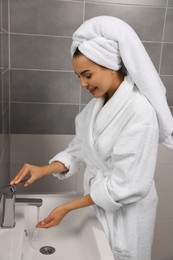 Photo of Beautiful young woman in bathrobe with towel on head washing hands at home