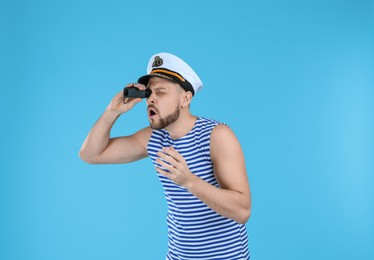 Sailor looking through monocular on light blue background