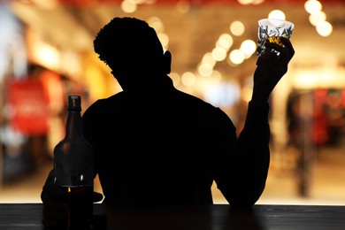 Silhouette of addicted man with alcoholic drink in bar