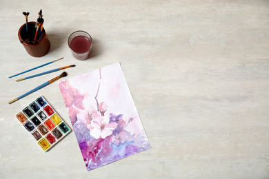 Flat lay composition with watercolor paints and floral picture on light table. Space for text