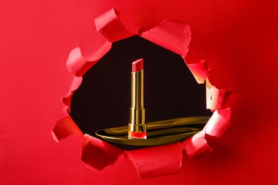 Bright red lipstick on gold plate, view through hole in paper