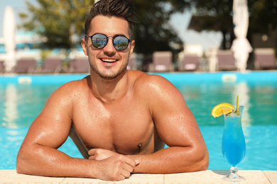 Young man wearing sunglasses with reflection of tropical beach in pool on sunny day 