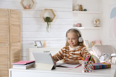 Cute little girl with modern tablet studying online at home, space for text. E-learning