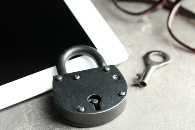 Vintage metal lock with key and tablet on grey table, closeup. Protection from cyber attack