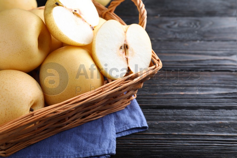 Photo of Cut and whole apple pears in basket on black wooden table, closeup