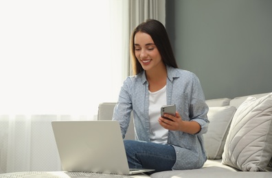 Woman with modern smartphone and laptop at home. Searching information