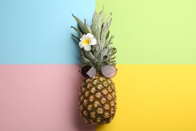 Pineapple with sunglasses and flower on color background, top view. Creative concept