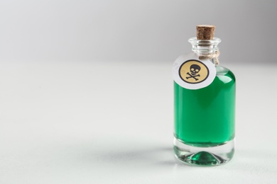 Glass bottle of poison with warning sign on light background. Space for text