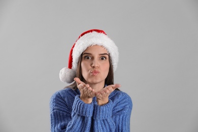 Pretty woman in Santa hat and blue sweater blowing kiss on grey background
