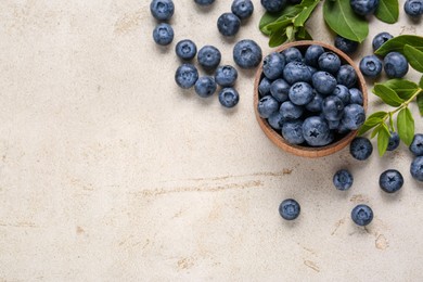 Tasty fresh blueberries and green leaves on light grey table, flat lay. Space for text