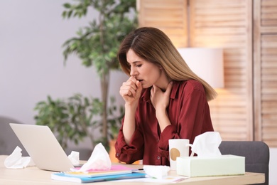 Sad woman suffering from cold while working with laptop at table