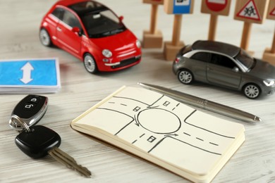 Composition with workbook for driving lessons and toy cars on white wooden background. Passing license exam