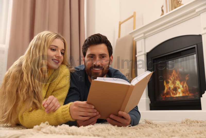 Lovely couple reading book near fireplace at home
