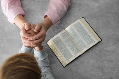 Boy and his godparent praying together at grey table, closeup