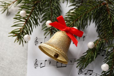 Photo of Golden shiny bell with red bow, music sheets and fir branches on light gray table, flat lay. Christmas decoration