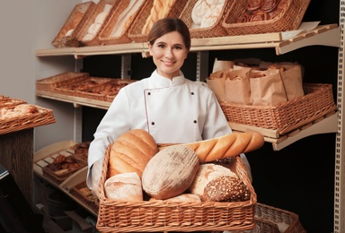 Professional baker with tray full of fresh breads in store