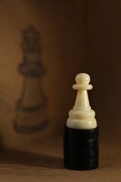 White pawn on wooden table in front of drawn queen chess piece
