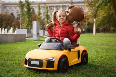 Cute little girl playing with toy bear and children's car in park
