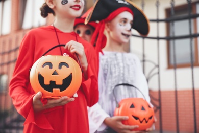Cute little kids with pumpkin candy buckets wearing Halloween costumes going trick-or-treating outdoors, closeup