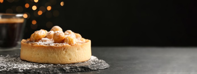 Image of Delicious tartlet with hazelnuts, sweet caramel and powdered sugar on black table, space for text. Banner design