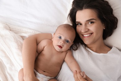 Happy young mother with her cute baby on bed, top view