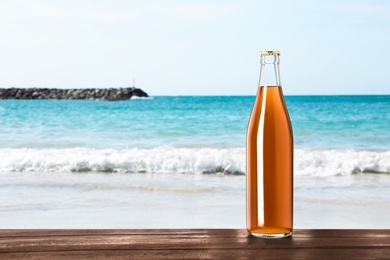 Bottle of delicious kvass on wooden table near sea. Space for text
