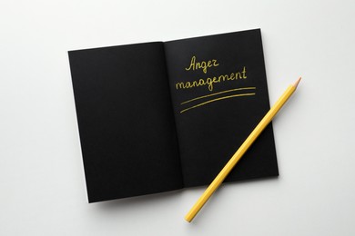 Black sketchbook with words Anger Management and pencil on white background, top view