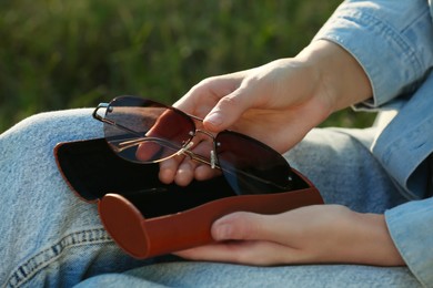 Photo of Woman holding sunglasses in brown leather case outdoors, closeup