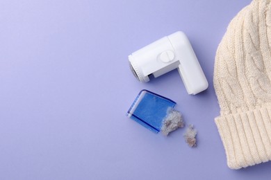 Photo of Fabric shaver with fuzz and knitted hat on lilac background, flat lay. Space for text
