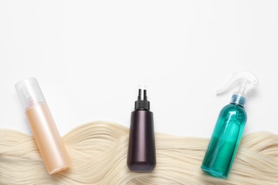 Photo of Spray bottles with thermal protection and lock of blonde hair on white background, flat lay. Space for text