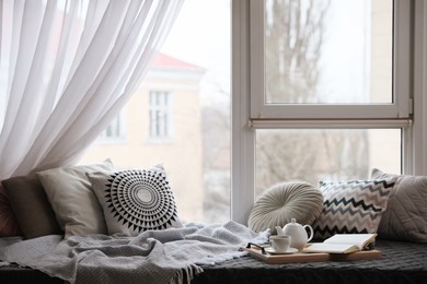 Comfortable lounge area with blanket and soft pillows near window in room