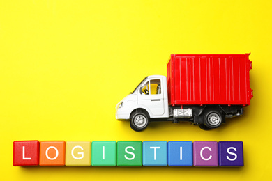 Flat lay composition with toy truck and word LOGISTICS on yellow background, space for text. Wholesale concept