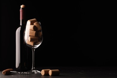 Photo of Bottle of wine, glass with corks and corkscrew on dark table. Space for text
