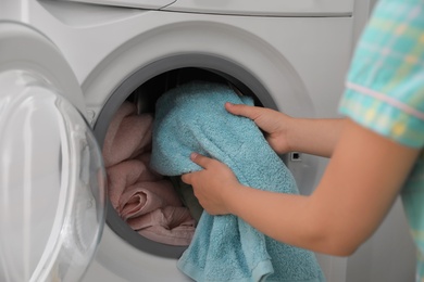 Woman putting dirty laundry into washing machine indoors, closeup