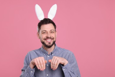 Photo of Happy man wearing bunny ears headband on pink background, space for text. Easter celebration