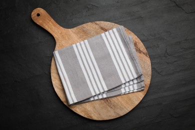 Striped kitchen towel and wooden cutting board on black table, top view
