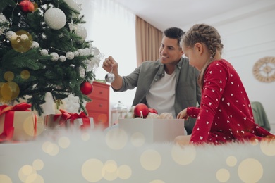 Father with his cute daughter decorating Christmas tree together at home