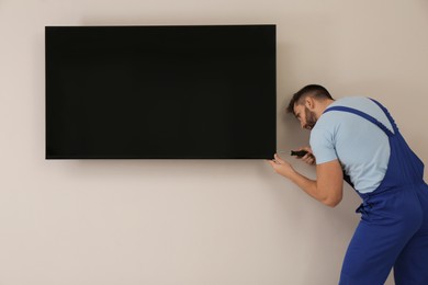 Photo of Professional technician with screwdriver installing modern flat screen TV on wall indoors