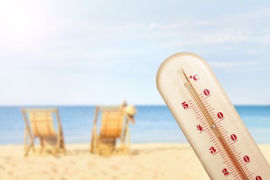 Weather thermometer and beautiful sandy beach with wooden sunbeds on background. Heat stroke warning